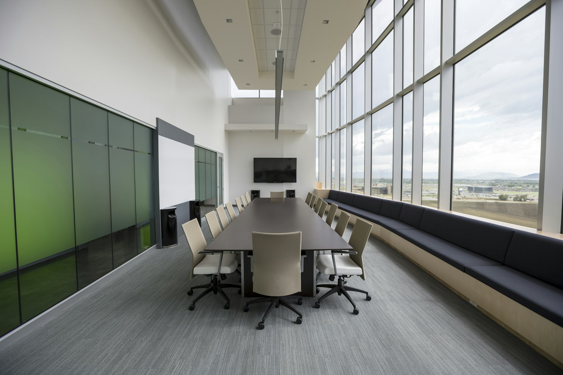 An empty modern boardroom with a long table and floor-to-ceiling windows.